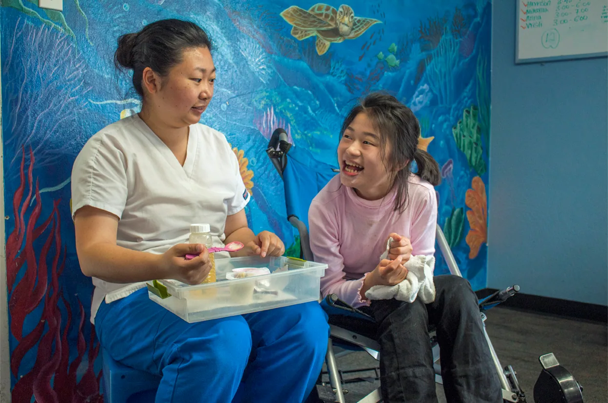 A nurse and a laughing girl in front of the ocean mural