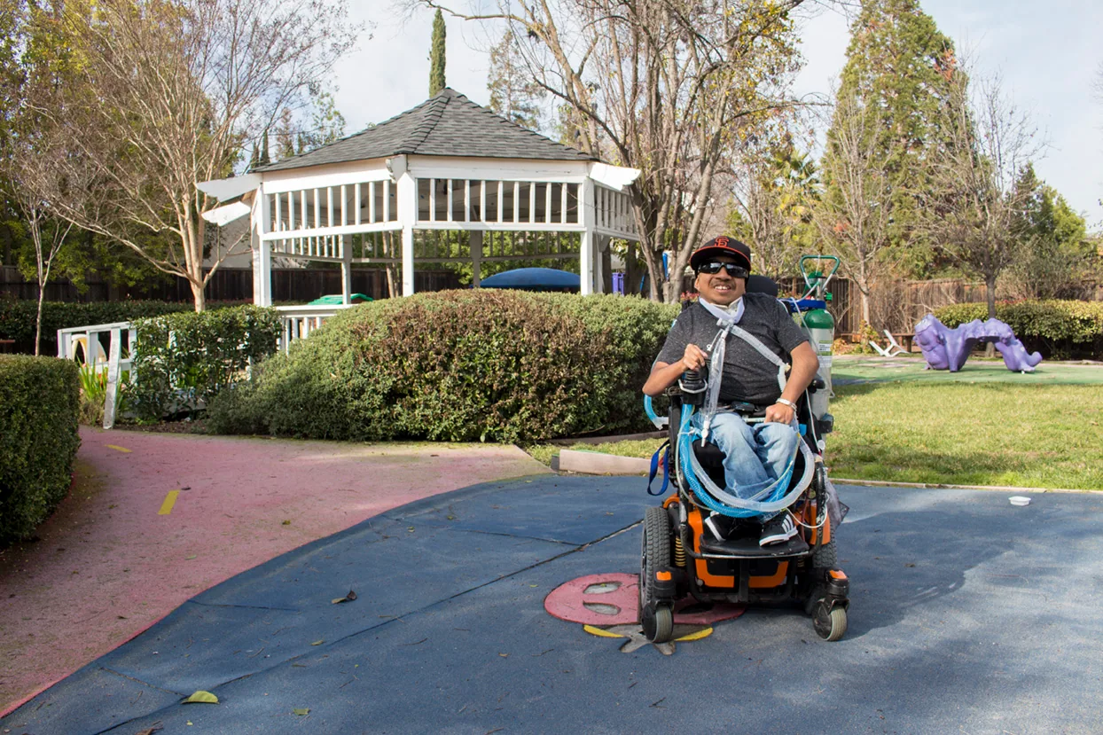 A young man in a power wheelchair on the playground path by the gazebo